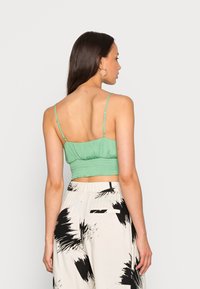 Top verde cortado com alças finas ajustáveis, costas franzidas e textura suave, combinado com calças largas estampadas em preto e branco.