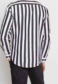 Zwart-witte verticaal gestreepte blouse met lange mouwen, knopen voor de manchetten en een gebogen zoom. Gemaakt van lichtgewicht stof met een casual pasvorm.