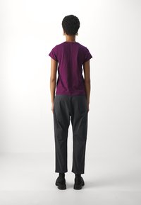 Camiseta de algodón morada de manga corta, combinada con pantalones grises de corte suelto y calzado negro, vista desde la parte trasera sobre un fondo blanco.