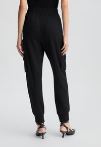 Pantaloni jogging neri con vita elastica, tasche cargo laterali e polsini affusolati. Texture liscia e materiale leggero.