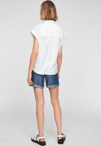 Camicia bianca a maniche corte con colletto, abbinata a jeans corti con risvolti, che mostrano una vestibilità comoda e un design casual.