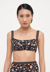 Marineblomstret crop-top med firkantet halsudskæring, tykke mønstrede stropper og orange accenter. Med et farverigt blomstermønster på en mørk baggrund.