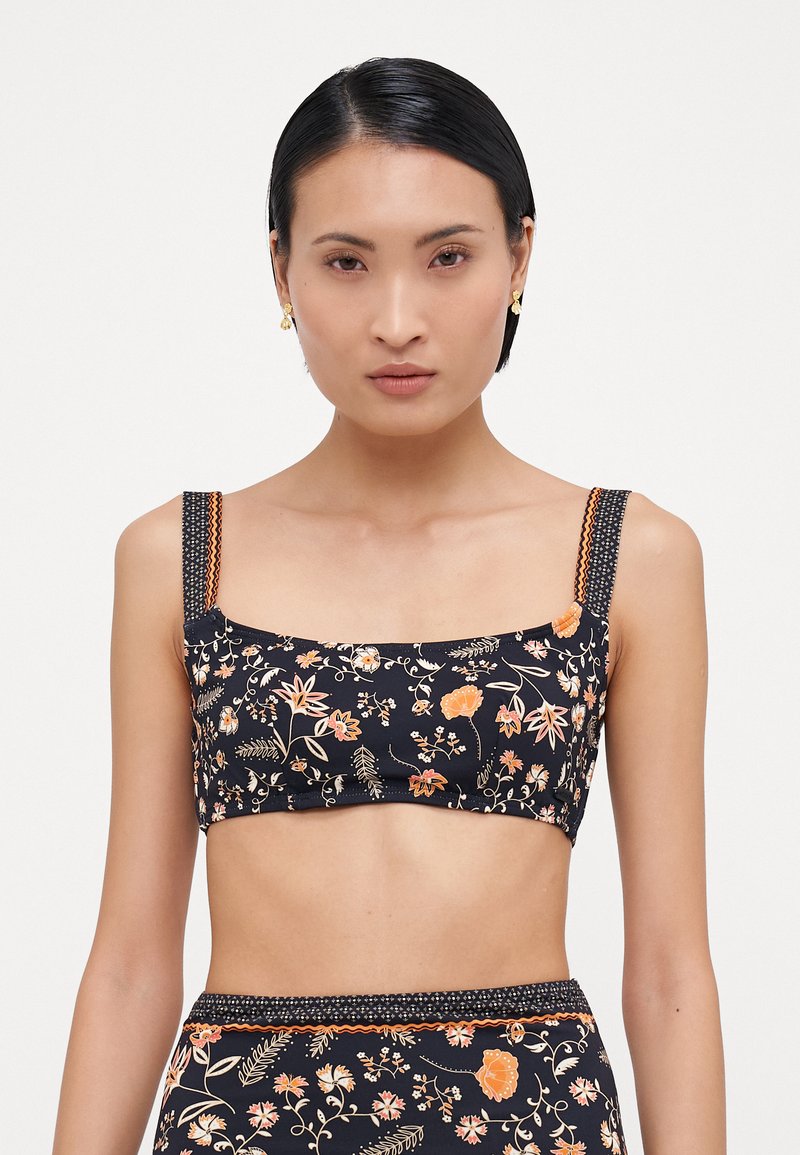 Marineblomstret crop-top med firkantet halsudskæring, tykke mønstrede stropper og orange accenter. Med et farverigt blomstermønster på en mørk baggrund.