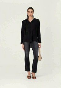 Black long-sleeve blouse, slim-fit dark jeans, and brown heeled sandals, paired with a small beige handbag, set against a neutral background.