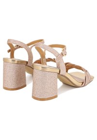 Scarpe con tacco glitter rosa con tacco spesso accentuato in oro, design open-toe e cinturini incrociati; il materiale testurizzato aggiunge interesse visivo.