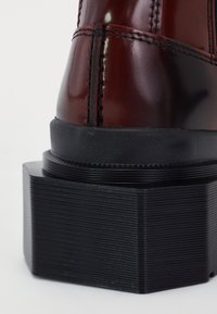 Gros plan sur une botte en cuir marron foncé avec une semelle plateforme épaisse et texturée noire et des coutures détaillées le long de la couture arrière.