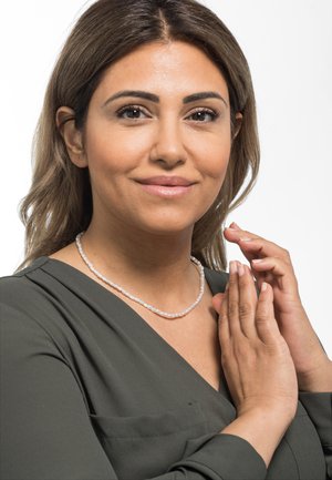 Collana di perle con piccole perle bianche rotonde indossata da una persona con una blusa verde scuro, mani delicatamente posizionate vicino all'area del collo.