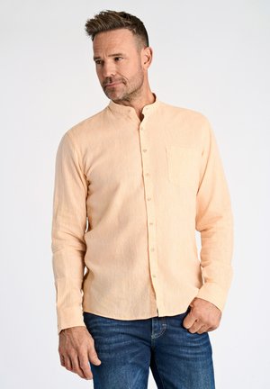 Camisa de manga larga naranja claro con cuello de mandarín, un bolsillo y cierre de botones, combinada con unos vaqueros azul oscuro. Textura suave.