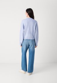 Lichtblauwe cropped sweater met geribbelde mouwen, gecombineerd met wijde denim jeans en witte sneakers, wat een casual, ontspannen look laat zien.