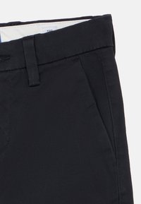 Σκούρο μπλε παντελόνι με θηλιές ζώνης και πλαϊνή τσέπη, που δείχνει την υφή του υφάσματος και μέρος της ετικέτας μεγέθους στο εσωτερικό της μέσης.