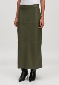 Olijf groene leren midi rok met een gladde textuur, voorzien van verticale naaddetails en een rechte silhouet, gecombineerd met zwarte stilettoboots.