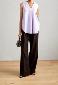 Laventelin väri slapptopp, jossa on V-muotoinen kaula-aukko, yhdistettynä korkeavyötäröisiin mustiin leveälahkeisiin housuihin. Pieni musta käsilaukku ja avokkaat.