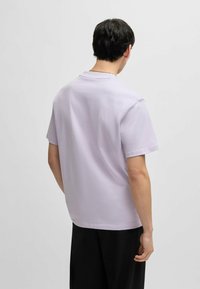 Tricou scurt cu mânecă scurtă de culoare lavandă deschisă, realizat din bumbac. Prezintă o croială lejeră și un decolteu rotund, cu o textură netedă și un design simplu.