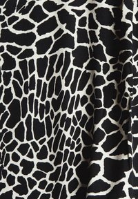 Tissu noir et blanc avec un motif imprimé girafe composé de formes irrégulières ; texture lisse avec un léger éclat.