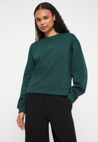 Felpa verde scuro con scollatura rotonda, maniche lunghe e orlo corto. Presenta un delicato design ricamato sul petto.