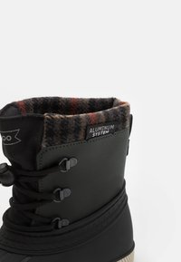 Vodotěsná černá gumová bota se zeleným syntetickým svrškem, filcovým límcem s šedou a červenou kostkou, nastavitelným šněrováním a štítkem "ALUMINUM SYSTEM".