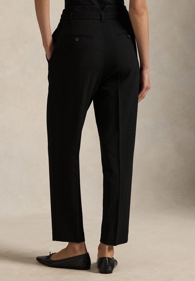 Melnas, piegrieztas taisnas griezuma bikses ar divām aizmugurējām kabatām un gludu faktūru. Komplektā ar melniem plakanām kurpēm, demonstrējot vienkāršu dizainu.