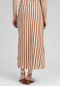 Jupe midi rayée marron et blanche avec une taille smockée et une coupe droite, assortie à des sandales à talons marron avec des brides autour de la cheville.