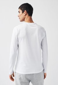 Långärmad T-shirt i vitt bomull, med en enkel design och rund halsringning, kombinerad med grå sweatpants med dragsko.