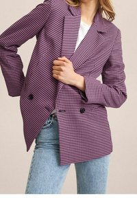 Blazer violet à motif pied-de-poule avec revers crantés, boutons croisés et coupe ajustée, associé à un jean bleu clair.