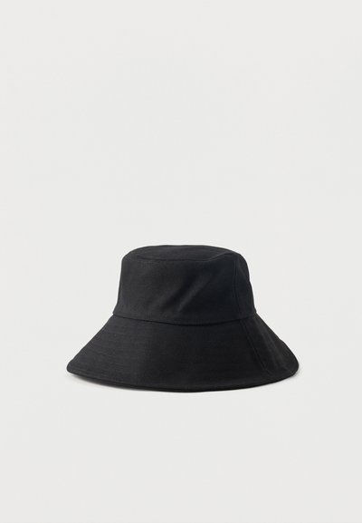 Μαύρο βαμβακερό καπέλο τύπου κουβά με φαρδιά, γωνιακή γείσο και δομημένη κορυφή, τοποθετημένο σε απλό ανοιχτό φόντο.
