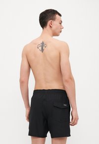 Svarte svømmebukser med elastisk midje og baklomme, med en glatt tekstur og minimalistisk design. Ingen synlige mønstre eller detaljer.