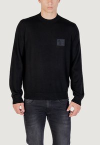 Maglione nero a maglia con colletto rotondo, polsini e orlo a costine, caratterizzato da una patch con logo tessurizzato nera sul lato sinistro del petto.