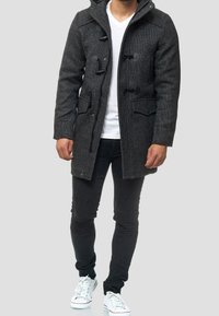 Mørkegrå hætte-dufflejakke med togglesystem, to frontlommer og et tekstureret stof. Kombinationen er med slim-fit sorte jeans og hvide sneakers.