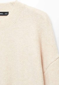 Pull en tricot beige avec un col rond, présentant des poignets et un ourlet côtelés. Texture douce avec une apparence légèrement duveteuse.