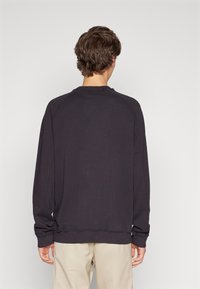 Sudadera negra de manga larga y cuello redondo. Presenta un corte holgado y puños acanalados. Textura suave; diseño minimalista.