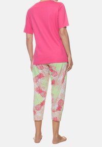 Lyserød kortærmet t-shirt parret med lette stofbukser, der har et livligt mønster af ananas og blade i pink, grøn og beige.