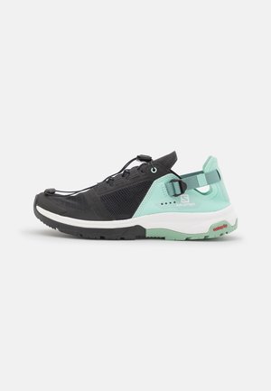 Zapatillas deportivas ligeras con parte superior de malla negra, acentos turquesas, suela flexible y correa en el talón ajustable para un ajuste seguro.