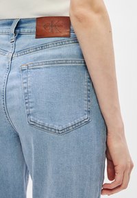 Ανοιχτό μπλε τζιν παντελόνι με καφέ δερμάτινη ετικέτα Calvin Klein. Διαθέτει κλασικό σχέδιο πέντε τσεπών και ελαφρώς φθαρμένη υφή.