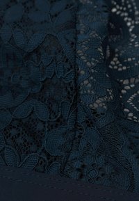 Marineblauwe kantstof met ingewikkelde bloemenpatronen en een gladde stevige marineblauwe onderlaag. De textuur is delicaat en gelaagd.