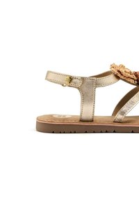 Sandal in pelle dorata con una fascia testurizzata e un dettaglio intrecciato decorativo. Suola marrone con una leggera battistrada per migliorare la presa. Presenta fibbie regolabili.