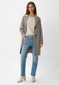 Beige Karomantel mit blauen und braunen Tönen, kombiniert mit einem leichten Strickoberteil und blauen Jeans. Eingerahmt von beigen Ankle-Boots mit Blockabsatz.