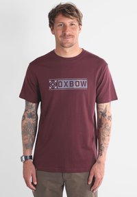 T-shirt en coton bordeaux avec un imprimé graphique comportant le texte "OXBOW" en bleu, col rond, manches courtes et ourlet droit.