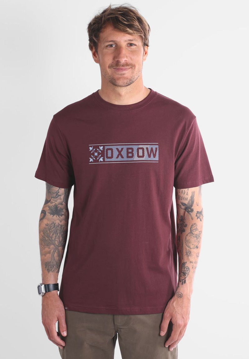 T-shirt en coton bordeaux avec un imprimé graphique comportant le texte "OXBOW" en bleu, col rond, manches courtes et ourlet droit.