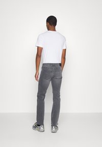 Gray denim jeans with a slim fit, five pockets, back yoke detail, paired with a white t-shirt and gray sneakers. Minimalist design.