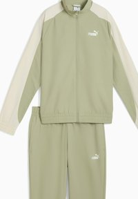 Lichtgroen trainingspak van gladde stof; jas met crèmekleurige accenten en ritssluiting, broek met elastische tailleband en zijzakken.