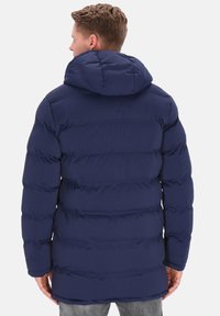 Marineblå dunjakke med horisontal syning, en stor hætte og et mellemlangt snit. Fremstillet af quiltet, isolerende stof for varme.