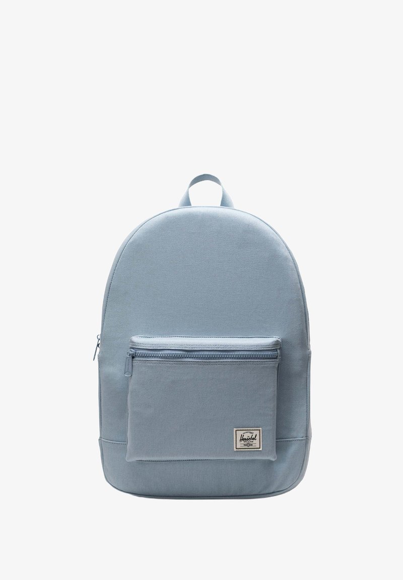 Vaaleansinisestä kankaasta valmistettu reppu, jossa on pyöreä muoto, etupuolella vetoketjullinen tasku ja päällinen kahva. Repussa on logo-tunnistus etutaskussa.