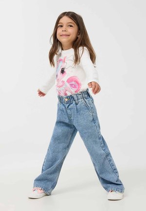 Jeans di denim azzurro chiaro con fit morbido e cintura elastica, abbinati a una camicia bianca a maniche lunghe con una grafica colorata di unicorno.