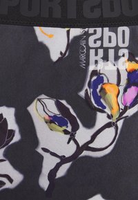 Tela con un colorido patrón floral que presenta acentos en púrpura, naranja y verde sobre un fondo negro, con una marca en la parte superior.