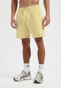 Lichtgele katoenen shorts met een elastische tailleband, zijzakken en een klein merklogo in de linkerbenedenhoek.