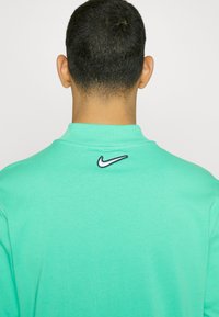 Mintgrön Nike sweatshirt med kort krage och en liten logotyp på baksidan, tillverkad av mjukt, texturerat material.
