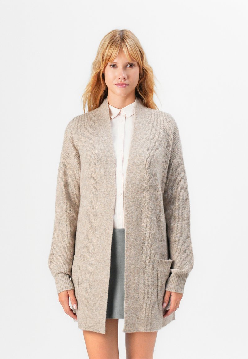 Beige Wollmischung Cardigan mit offenem Vorderteil, gerippter Textur, Seitentaschen und langen Ärmeln. Kombiniert über einem leichten Hemd und einem Rock.