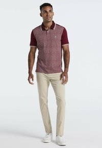 Bordeaux polo shirt met een gestructureerd patroon en witte kraagstrepen, gecombineerd met lichtbeige broek en witte sneakers.