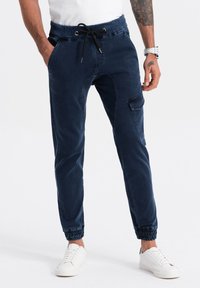 Pantalones jogger de color marino, hechos de tela suave, con cintura elástica, cierre de cordón, bolsillos laterales y puños elásticos. Textura suave con un brillo sutil.