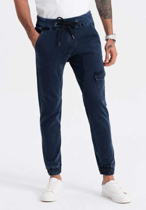 Pantalones jogger de color marino, hechos de tela suave, con cintura elástica, cierre de cordón, bolsillos laterales y puños elásticos. Textura suave con un brillo sutil.